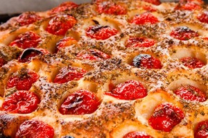 Focaccia barese originale in teglia di ferro blu con pomodorini e origano